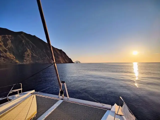Un catamarano davanti a una costa scura, al tramonto