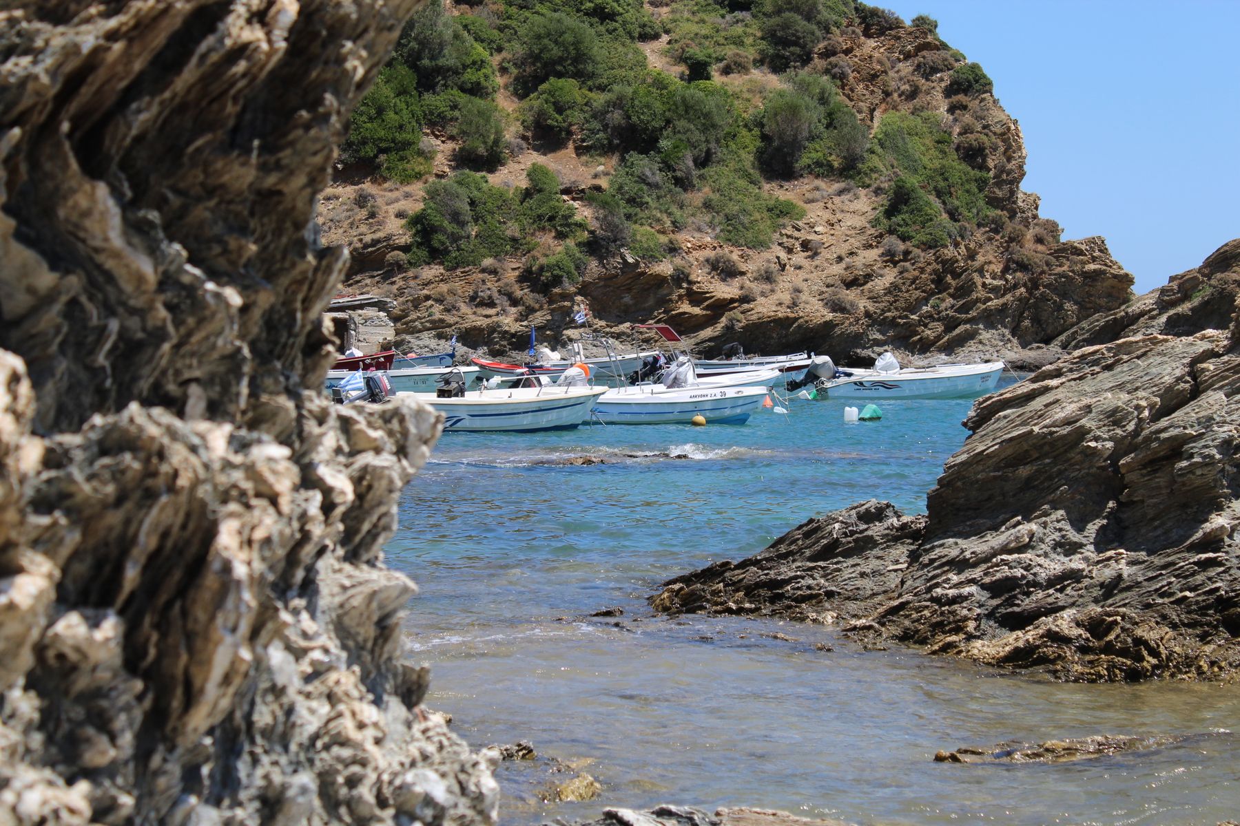 Piccole barche a motore all'ancora in una baia riparata dalle rocce, con acqua trasparente