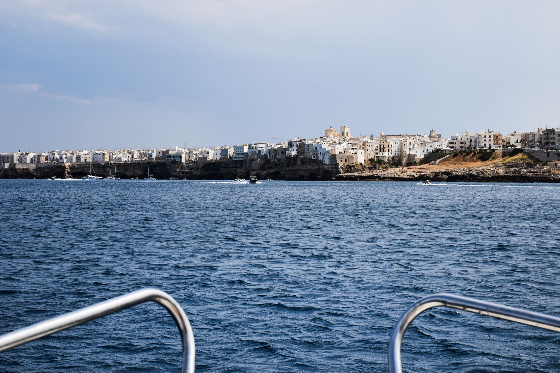 Una costa alta e rocciosa vista dal mare in navigazione, con l'acqua trasparente ai piedi delle scogliere